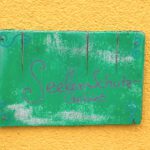 Körpertherapie Psychotherapie Freiburg Ettenheim Heilpraktikerin Praxis (2) Grüne Holztafel auf der gelben Hauswand der Praxis für Körpertherapie in Ettenheimweiler